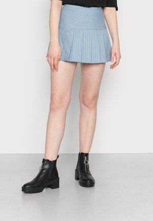 Saia mini plissada azul clara com riscas verticais, combinada com botas de tornozelo pretas, com sola robusta e detalhes em zíper.
