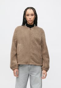 Bruine, pluizige fleecejas met een rits aan de voorkant, geribde kraag en zijzakken. Heeft een ontspannen pasvorm en elastische manchetten.