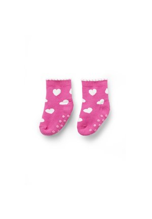 Petites chaussettes roses pour tout-petits avec motifs de cœurs blancs et semelles antidérapantes posées à plat sur un fond blanc.