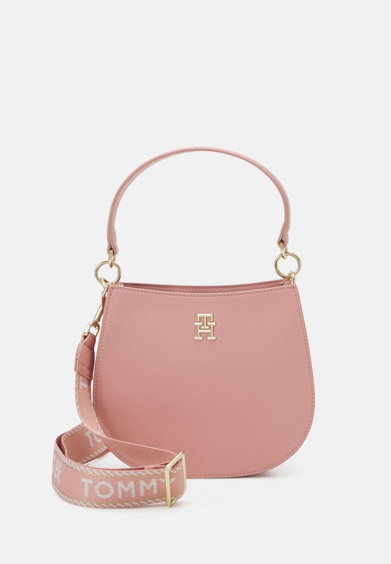 Růžová kožená kabelka s křivolakým tvarem, zlatým kováním a odnímatelným popruhem s nápisem "TOMMY" a tkanými doplňky.