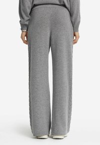 Pantalons larges tricotés gris clair avec des détails en tricot torsadé sur les côtés, présentant une finition texturée et une taille élastique.