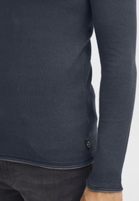 Camicia a maniche lunghe blu navy in tessuto strutturato con una forma aderente. Presenta un collo a giro e un piccolo logo etichetta vicino all'orlo.