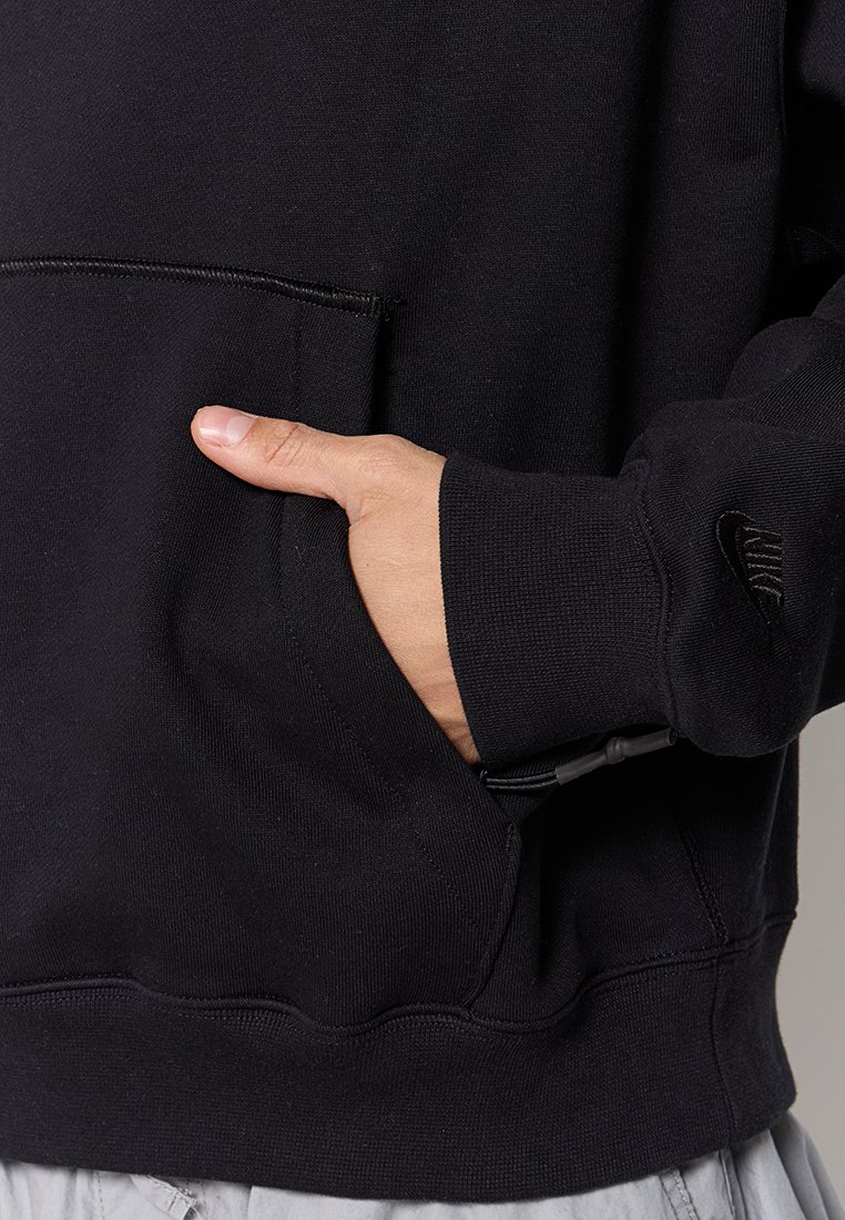 Schwarzer Sweatshirt mit einer vorderen Kängurutasche, gerippten Bündchen und einem kleinen Logo am Ärmel. Hergestellt aus weichem Stoff mit strukturierter Oberfläche.