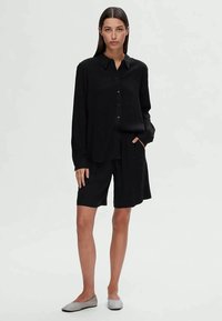 Black long-sleeve shirt with buttons, paired with black shorts. The outfit features a relaxed fit and a smooth fabric texture.