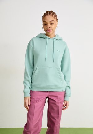 Mint green hooded sweatshirt with a front pocket, ribbed cuffs, and a small logo. Paired with pink pants. Simple, relaxed design.