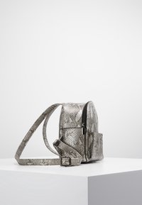 Mochila de estampado de serpiente en gris con un compartimento con cremallera y correa ajustable. Fabricada con material sintético texturizado. Incluye un bolsillo frontal.