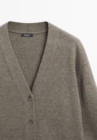 Khaki cardigan z jemné vlněné směsi, s hlubokým výstřihem do V, dvěma černými knoflíky a texturovaným pleteným vzorem.