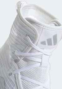 Valkoinen korkeavartinen urheilukenkä, jossa on teksturoitu verkkopäällinen, sileät synteettiset yksityiskohdat ja litteät valkoiset nauhat, joissa on vetokahva kannassa.