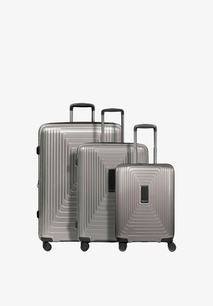 Trois valises rigides argentées métalliques de tailles variées avec poignées télescopiques et quatre roues pivotantes, disposées côte à côte.