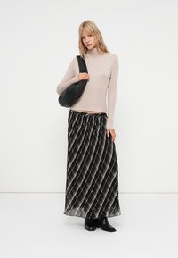 Bež majica z dolgimi rokavi in turtleneck ovratnikom, v kombinaciji z maxi krilom v črno-beli črtasti zasnovi. Krilo ima plisirano teksturo in črne gležnjarje.