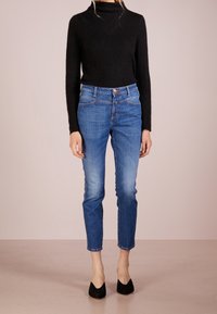 Suéter negro de cuello alto combinado con jeans azules hasta los tobillos. Los jeans tienen un diseño clásico de cinco bolsillos y un ligero desvanecimiento en las piernas. Tacones negros.