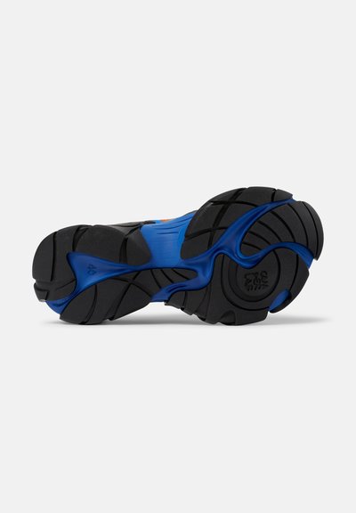 Schwarze und blaue Sport- Schuhsohle aus strukturiertem Gummi mit Wellenmuster, ausgeprägten Traktionsrillen und Logodetails.