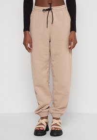 Beige Sweatpants mit elastischem Bund, Kordelzug und Bündchen an den Knöcheln, kombiniert mit klobigen schwarzen Sandalen mit einer beigefarbenen Schnalle.