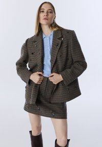 Blazer marrón de escocés con adornos azules, combinado con una falda a juego. Suéter de punto azul claro y acogedor debajo.