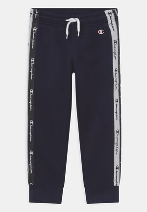 Pantalones deportivos azul marino con cordón y franjas laterales negras y grises que muestran logos repetidos de Champion y un pequeño emblema de Champion en la cadera.