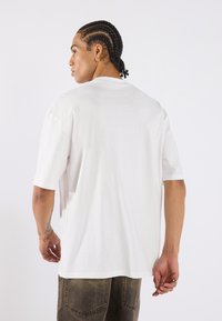 White short-sleeve t-shirt with a crew neckline, relaxed fit, and smooth texture, paired with dark, faded baggy pants.