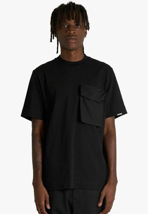 Maglietta nera in cotone con maniche corte, scollo rotondo e tasca frontale con patta. Design semplice con una vestibilità comoda.