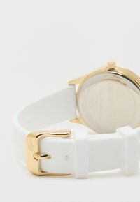 Balts silikona siksniņas pulkstenis ar zelta toni. Apaļa korpusa forma, gluda aizmugure un teksturēta siksniņa. Satur logotipa detaļu.