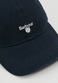 Marineblauwe katoenen pet met een geborduurd "Barbour"-logo en schild. Het ontwerp heeft een gebogen klep en zichtbare stikseldetails.
