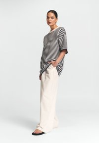 Riba lühikeste varrukatega särk tumesinises ja kreemjas värvitoonis, koos kreemjate laiade pükstega. Mudel seisab, käsi taskus, jalas on mustad sandaalid.