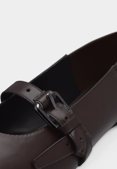Chaussure Mary Jane en cuir marron foncé avec un bout arrondi et une bride réglable munie d'une boucle en métal noir.