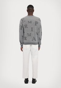 Grå stickad tröja med stora mörka bokstäver utspridda. I kombination med vita byxor och svarta skor. Enkel krage och ribbade ärmslut.