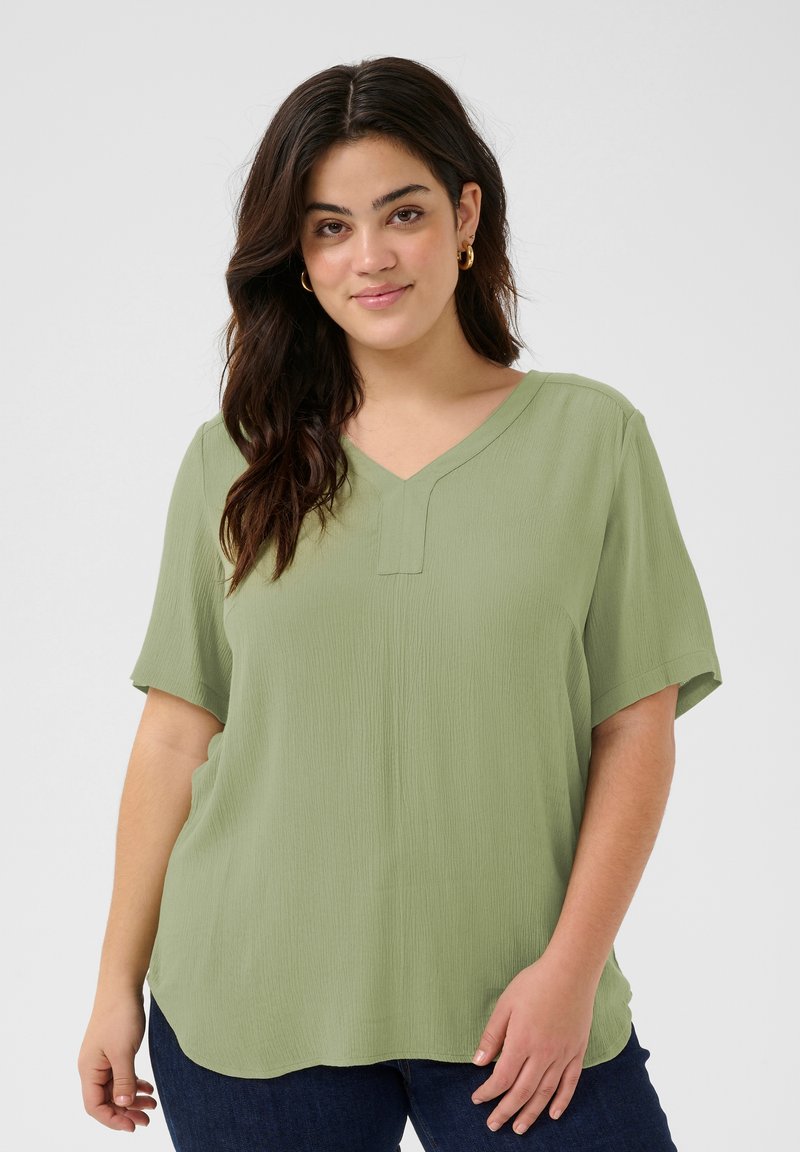 Blusa corta a maniche corte verde oliva con scollatura a V, realizzata in tessuto strutturato, caratterizzata da un orlo dritto e una vestibilità rilassata.