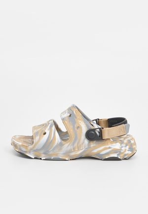 Beige og grå marmor-åben-tå-sandal med to remme og en sort og beige justerbar hælrem på en hvid baggrund.