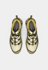 Πράσινα και μπεζ αθλητικά παπούτσια με διχτυωτό ύφασμα, λαστιχένιες σόλες και μαύρα κορδόνια. Διαθέτουν λογότυπο στο πλάι και επένδυση με μαξιλαράκι εσωτερικά.