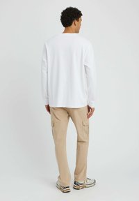 Chemise blanche à manches longues avec un col rond, associée à un pantalon cargo beige avec des poches latérales et une coupe décontractée. Baskets multicolores.