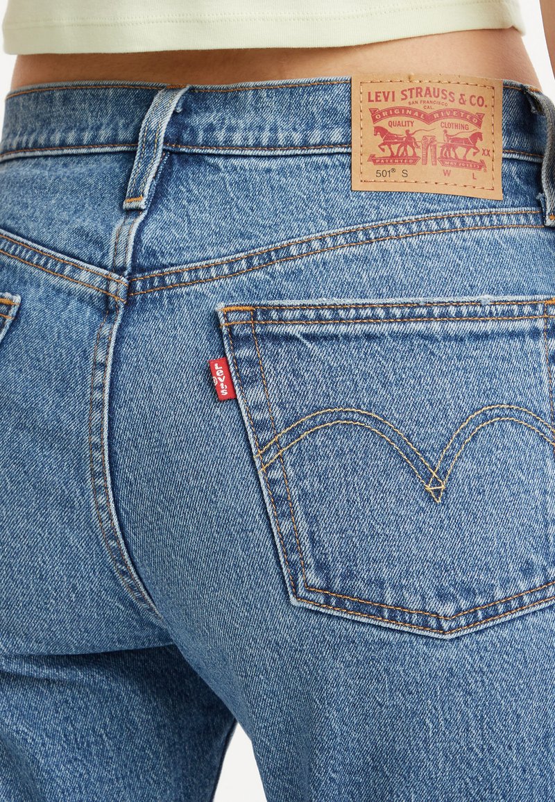 Hellblaue Jeans aus Denim mit hohem Bund. Enthält ein Leder-Logo-Patch und ein kleines rotes Etikett; die hinteren Taschen haben eine gebogene Naht.