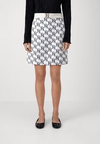 Biała spódnica o strukturalnym kroju z czarnym geometrycznym wzorem, z białym paskiem z złotą klamrą, zestawiona z czarnymi lakierowanymi balerinami.