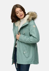Jasnozielona kurtka parka z kapturem wyłożonym futrem, kołnierzem z kremowego polaru, zamkiem z przodu oraz kieszeniami na zatrzask. Teksturowana powierzchnia materiału.