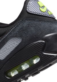 Gros plan du talon d'une chaussure noire Nike Air Max avec un coussin d'air visible et des matériaux en daim et en tissu texturés.