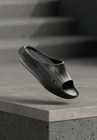 Μαύρο παπούτσι slip-on με ανοιχτό toe, με λεία υφή και ριμπά πλευρικό σχέδιο, συμπληρωμένο από μια διακριτική λεπτομέρεια λογότυπου.
