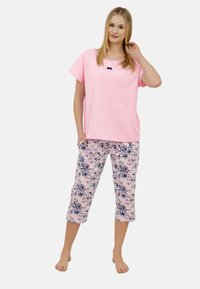 Różowa bluzka z krótkim rękawem i małą granatową kokardą, w połączeniu z krótkimi spodniami w kwiatowy wzór w pastelowych kolorach, wykonanymi z miękkiej bawełny.