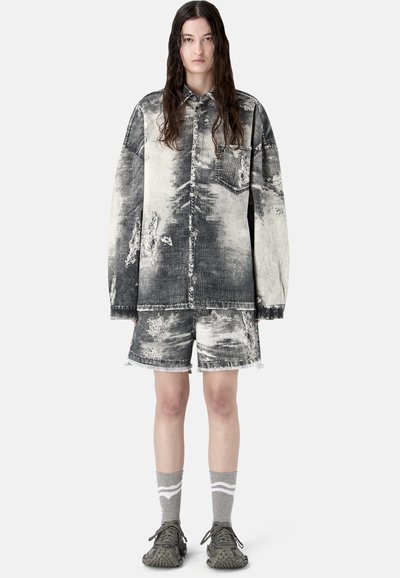 Person trägt eine übergroße schwarze und weiße, mit Säure gewaschene Denimjacke und passende Shorts, graue gemusterte Socken und strukturierte graue Turnschuhe.