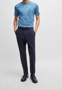 Blå mönstrad t-shirt i mjukt tyg, i kombination med marinblå byxor med dragsko i midjan och eleganta svarta skor.