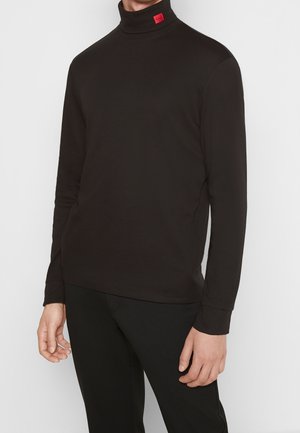 Mężczyzna ubrany w czarny, długi rękaw z golfem z małą czerwoną metką na kołnierzu, w połączeniu z czarnymi spodniami, na białym tle.