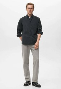 Camisa negra de botones, jeans grises de pierna recta y zapatos negros. La camisa tiene mangas largas y un corte relajado. Textura sutil, diseño simple.
