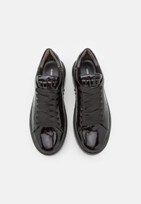 Zwarte lakleren sneakers met ronde neus, gestructureerde zwarte veters en een gladde afwerking. Merken zichtbaar op de binnenzool.