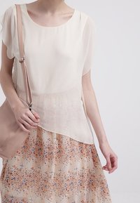 Kermansävyinen sifonkinen pusero, jossa liehuvat hihat, yhdistettynä kukkakuvioiseen, läpikuultavaan hameeseen, jossa oransseja ja sinisiä yksityiskohtia. Vaaleanpunainen olkalaukku.