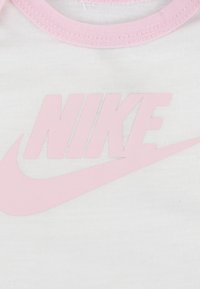 Λευκό βαμβακερό μπλουζάκι με ελαφρώς ροζ στρογγυλή λαιμόκοψη και μεγάλο ροζ λογότυπο "NIKE" μπροστά, με λεία υφή υφάσματος.