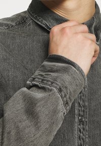 Grå denimskjorta med klassisk krage, knappstängning fram och textil med synlig söm och ärmdetalj.