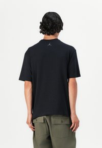 Sort kortærmet t-shirt med rund hals og diskret Jordan-logo i sort på bagsiden. Lavet af bomuldsstof, afslappet pasform.