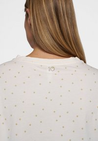 Hvid T-shirt med spredte guldprikker og et lille "10" broderet ved nakken bagpå. Blødt, bomuldsmateriale.