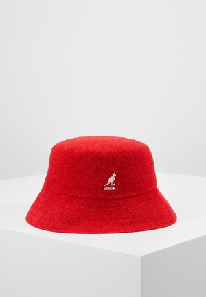 Cappello a secchiello rosso realizzato in tessuto testurizzato, con logo Kangol sul davanti. Il design presenta una corona arrotondata e una visiera larga che scende verso il basso.