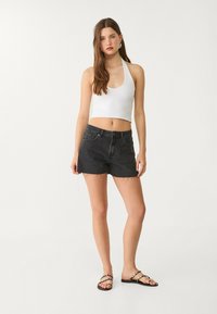 Bijela halter crop majica u kombinaciji s crnim trapericama s rasporenim rubovima i točkicama, upotpunjena crnim ravnim sandalama.