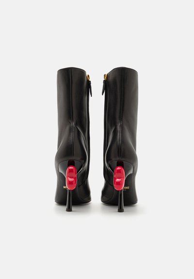 Black leather ankle boots with a high, slender heel featuring a red accent. Gold zipper detail at the back and logo on the sole.