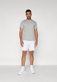 Grå kortærmet t-shirt med rund krave, parret med hvide sports shorts. Stoffet virker let; skoene er hvide sneakers.